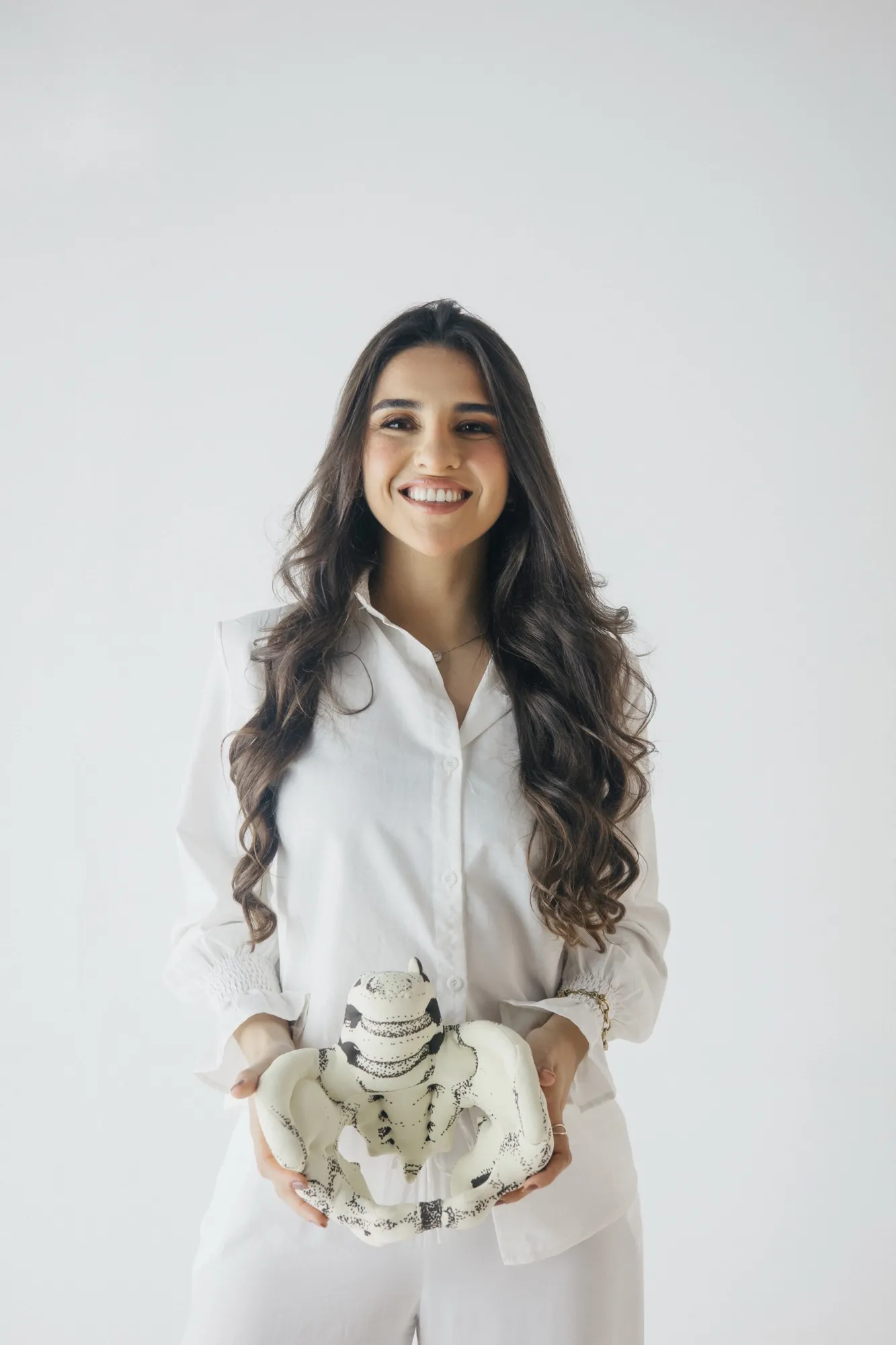 Thaynara Brito, fisioterapeuta, sorrindo e segurando um modelo anatômico de pelve
