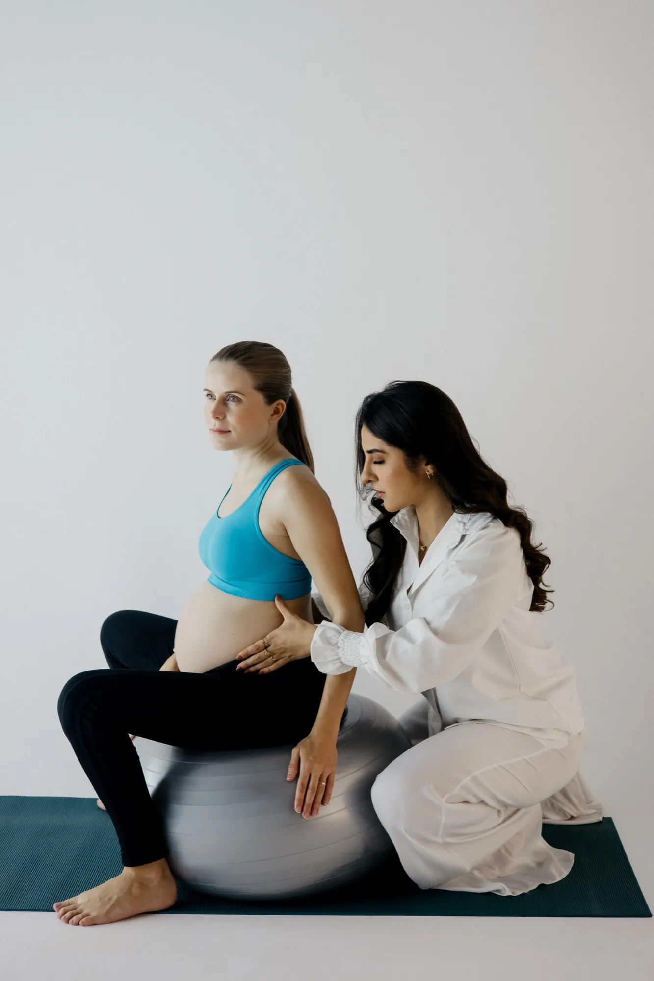 Thaynara ajusta a postura de uma gestante sentada na bola de Pilates