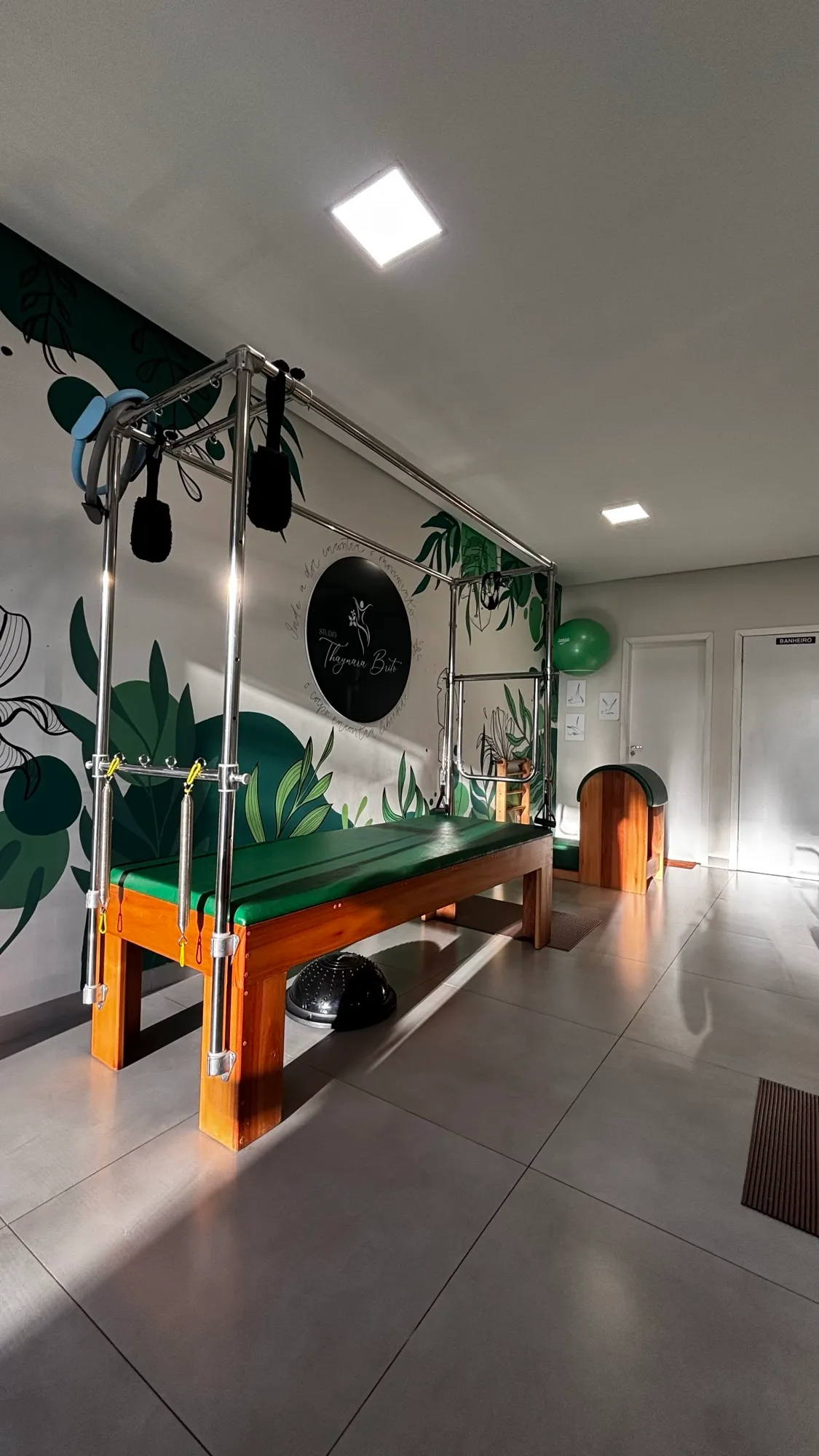 Cadillac de Pilates no studio, com a parede de folhagens verdes e o logo Studio Thaynara Brito